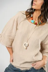 Blusa beige de lino con mangas 3/4 con lazos y detalle de flecos en los puños.