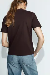 Camiseta de cuello redondo y manga corta en color marrón oscuro, con detalle de aplicaciones de perlas distribuidas en el cuello y en el ruedo.