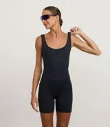 Enterito deportivo corto de microfibra color negro, con breteles anchos, escote redondeado y bolsillos laterales funcionales. Presenta costuras estratégicas en el busto y cintura, con un diseño de espalda con recorte central.