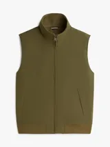 Chaleco verde militar Tommy Hilfiger de cuello alto, con cierre frontal de cremallera y dos bolsillos laterales de ojal. Presenta un diseño sin mangas con logo monotipo bordado en el pecho.