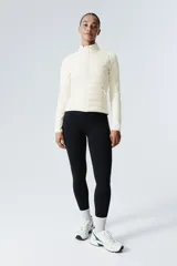 Campera híbrida color crema, con cuerpo acolchado y mangas de tejido elástico. Presenta cuello alto, cierre frontal y bolsillos laterales con cierre.