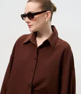 Camisa de corte oversized con estilo sastre, confeccionada en tejido plano. Presenta cuello clásico, cierre frontal con botones, mangas largas con puños anchos y sisas desplazadas.