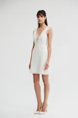 Vestido corto de color blanco con escote en V pronunciado, detalles de encaje en el torso y tirantes anchos con apliques. Presenta una falda corta de encaje con diseño recto.