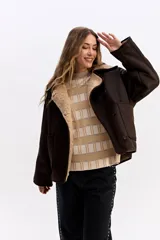 Campera de estilo aviador en color marrón oscuro, con exterior efecto gamuza e interior de corderito sintético color beige. Presenta cuello amplio, cierre frontal con botones y bolsillos laterales.