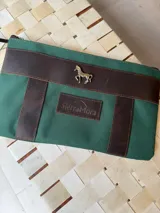 Sobre o cartuchera de lona fucsia con terminaciones y detalles de cuero marrón. Cuenta con cierre superior y aplique metálico de caballo en la parte frontal, además de una etiqueta de cuero con la marca grabada.