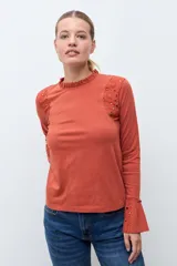 Remera de manga larga color terracota, con cuello alto y detalles de broderie en los hombros y puños acampanados.