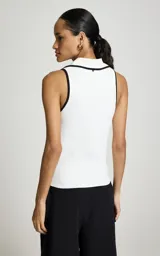 Top polo Pat de la marca Le Lis Blanc, de tejido acanalado en color blanco con detalles de ribetes negros en el cuello y la solapa. Presenta un diseño sin mangas, corte al cuerpo y escote en V profundo con cuello tipo polo.