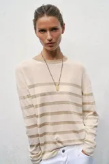 Jersey de punto de cuello redondo y manga larga, con diseño de rayas horizontales en tono metalizado sobre base color crema.