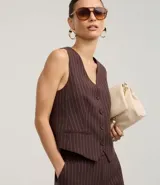 Chaleco entallado de mujer, color marrón oscuro con finas rayas verticales blancas (rayas de giz). Presenta escote en V, cierre frontal con botones forrados y bolsillos falsos.