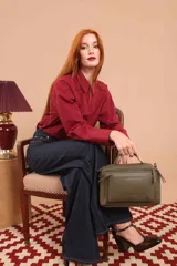 Bandolera de diseño rectangular en color verde oliva, confeccionada en material sintético. Cuenta con un asa superior rígida, correa larga ajustable y extraíble, y dos bolsillos frontales con cierre metálico. Presenta el logo de la marca grabado en el frente.