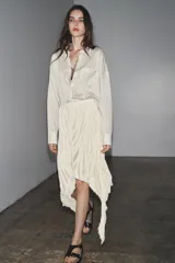 Falda midi color crudo, de tiro medio y confeccionada en viscosa. Presenta detalle de pliegues y bajo asimétrico. Cierre lateral con cremallera oculta.