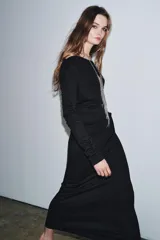 Vestido largo de color marrón oscuro, con cuello fluido tipo bote, manga larga y detalle de fruncido lateral con broche metálico en la cintura.