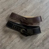 Cinto ancho de cuero negro con hebilla metálica dorada y tachas doradas.