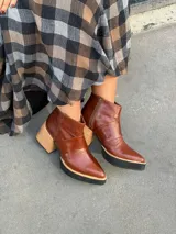Botinetas de cuero color marrón con punta fina, cierre lateral y suela con plataforma de goma negra y taco cuadrado de madera clara.