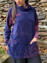 Polerón de plush azul con efecto batik en tonos rojizos, cuello alto holgado, mangas largas raglán, bolsillos frontales tipo parche y aberturas laterales para lactancia con dobladillo trasero más largo.