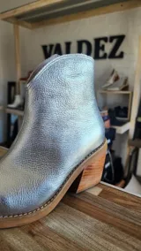 Botas tejanas de cuero charolado negro, con taco cuadrado de 7 cm y punta fina. Cuentan con cierre interno y costuras visibles en la suela.