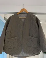 Casaca acolchada de diseño matelassé en color gris visón, con cuello redondo, cierre frontal abierto y dos bolsillos frontales de parche.