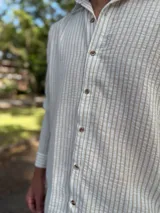 Camisa de lino blanca con rayas verticales beige, de manga larga, cuello camisero y cierre frontal de botones.