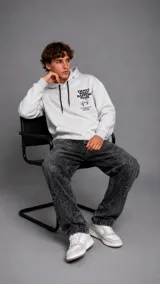Hoodie gris jaspeado con capucha y cordones negros ajustables. Presenta un estampado gráfico en el pecho con texto y diseño artístico.