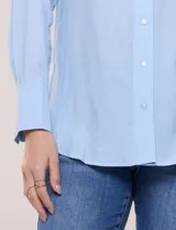 Camisa de calce relajado color celeste, confeccionada en tejido de textura suave y fluida. Presenta cuello camisero y abotonadura frontal, mangas largas con puño ancho y ruedo curvo.