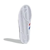 Championes Adidas Superstar blancos con detalles en azul y rojo. Presentan las tres tiras características de Adidas en los laterales en azul y rojo, y refuerzo de talón en rojo con la palabra "STAR" en blanco. La puntera es de goma con textura.