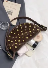 Bolso pequeño de hombro con forma de media luna, color negro, decorado con tachas redondas doradas. Cuenta con una correa ajustable y herrajes dorados.