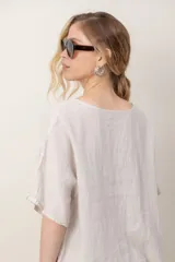 Blusa de lino color blanco, de corte amplio, con escote redondo, mangas cortas y detalle de guarda calada horizontal en la parte inferior.