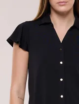 Camisa de seda fría blanca con cuello solapa, escote en V y cierre frontal de botones. Cuenta con mangas cortas con volados.