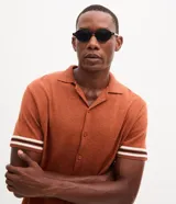 Camisa de punto jacquard color naranja, con cuello solapa, manga corta y cierre frontal con botones. Presenta detalles de rayas horizontales en contraste en el ruedo y en los puños de las mangas.