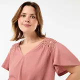 Camiseta rosada de manga corta con escote en V, confeccionada en tejido texturizado con detalles de encaje y macramé en los hombros.