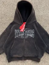 Campera canguro con cierre frontal, capucha y bolsillos tipo canguro, en tono marrón con efecto gastado vintage y estampa gráfica blanca con detalles de strass en el pecho.