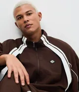 Campera deportiva de poliamida color marrón con detalles en blanco en los hombros y mangas. Presenta cierre frontal completo, cuello alto y puños elásticos.