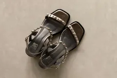 Sandalia de cuero color bronce metalizado, con punta cuadrada, taco ancho y bajo, y tiras finas adornadas con tachas esféricas plateadas.