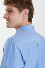 Camisa de vestir blanca de manga larga, con cuello abotonado, bolsillo frontal y botones en tono madera.