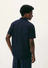 Camisa de manga corta con cuello clásico, cierre frontal de botones y bolsillo en el pecho. Presenta un corte entallado y un acabado de textura sutil.