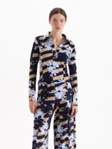 Remera de manga larga con cuello polo y cierre frontal parcial. Presenta un diseño estampado que combina rayas horizontales en tonos azul marino y tostado con un motivo floral en celeste.