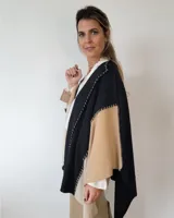 Ruana de lana color negro, beige y tostado, con diseño geométrico y flecos en el borde inferior.