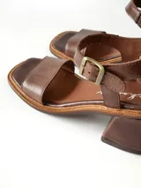 Sandalias de cuero color chocolate, con taco cuadrado de 6 cm, tira ancha en la parte delantera y tira en el tobillo con hebilla metálica ajustable.