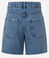 Short midi de jean azul con tiro medio, bolsillos frontales y traseros, trabillas para cinturón y detalle de tachas metálicas aplicadas en los laterales y bolsillos. El diseño se completa con un dobladillo deshilachado.