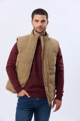 Chaleco reversible acolchado con diseño capitoneado. Un lado presenta un acabado en color beige con cierre frontal y bolsillo vertical en el pecho, mientras que el otro lado es de color azul marino. Cuenta con cuello alto y relleno térmico para mayor abrigo.