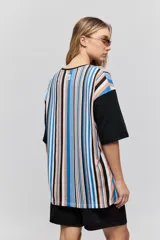 Remera oversize de manga corta con diseño de rayas verticales en tonos rojos, negros, blancos y tostados, y mangas blancas lisas.