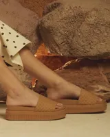 Sandalias tipo ojotas color habano con faja ancha superior de textura tejida y suela de plataforma alta texturizada.