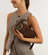 Cartera tipo baguette mediana en PU color marrón, con diseño alargado y asa corta para el hombro. Presenta un detalle frontal de cinturón con hebilla metálica y ojalillos.