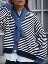 Sweater de punto a rayas horizontales blancas y azul marino, con cuello redondo, cierre frontal con botones y mangas largas con puños y detalles en tono azul.