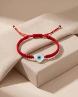 Pulsera de hilo rojo en macramé con dije en forma de corazón de nácar con diseño de ojo turco. Cuenta con cierre regulable con esferas plateadas en las terminaciones.