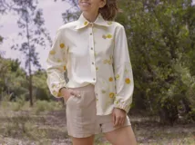 Camisa blanca con estampado de hojas en tonos beige y verde, cuello camisero, mangas largas con lazos en los puños y botones de madera.