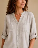 Camisa de lino color beige, de corte holgado, con cuello mao, bolsillos frontales en el pecho, mangas largas remangables y cierre frontal con botones.