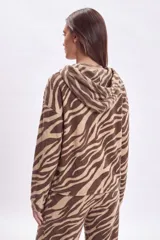 Canguro con capucha y cordones ajustables, confeccionado en lanilla con estampado animal print tipo cebra en tonos marrón y beige. Presenta mangas largas con puños elásticos y un corte holgado.