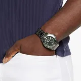 Reloj analógico Guess con caja de acero inoxidable en tono gris gunmetal y esfera verde. Presenta un diseño deportivo con bisel giratorio, índices luminiscentes y malla de eslabones de acero con acabado cepillado.