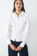 Camisa de manga larga confeccionada en popelina de algodón. Diseño de corte recto con cuello clásico, cierre frontal oculto y puños anchos con botón.